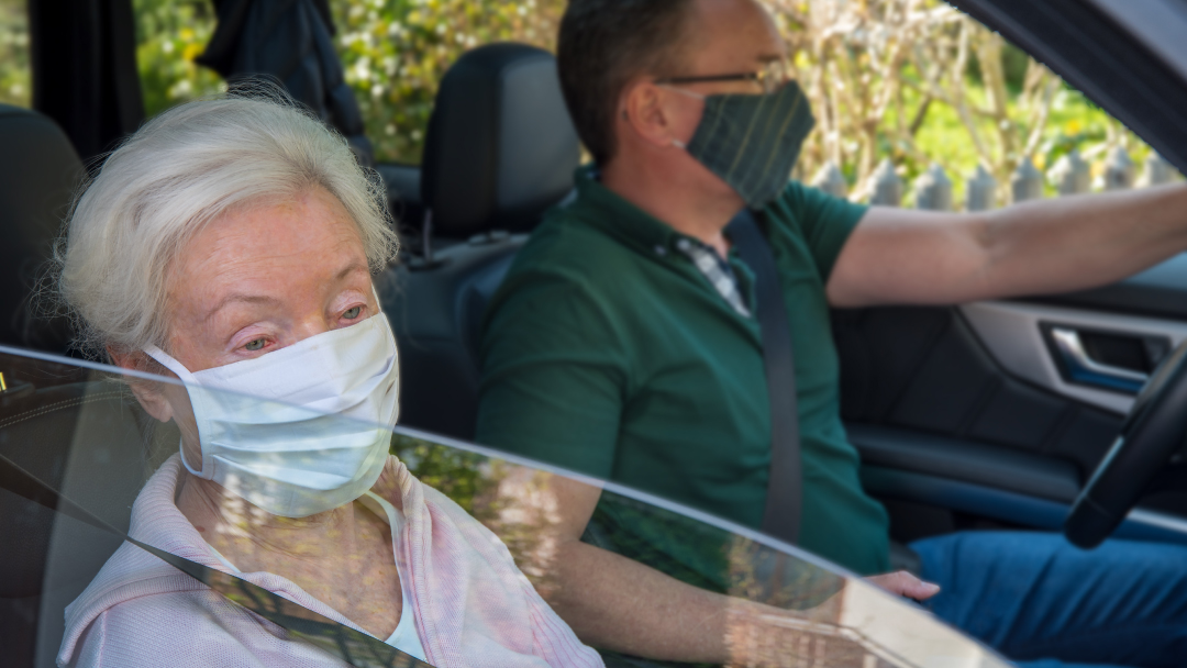 Masked male volunteer drives older woman passenger